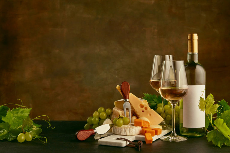 Front view of tasty cheese plate with the wine bottle on dark studio background
